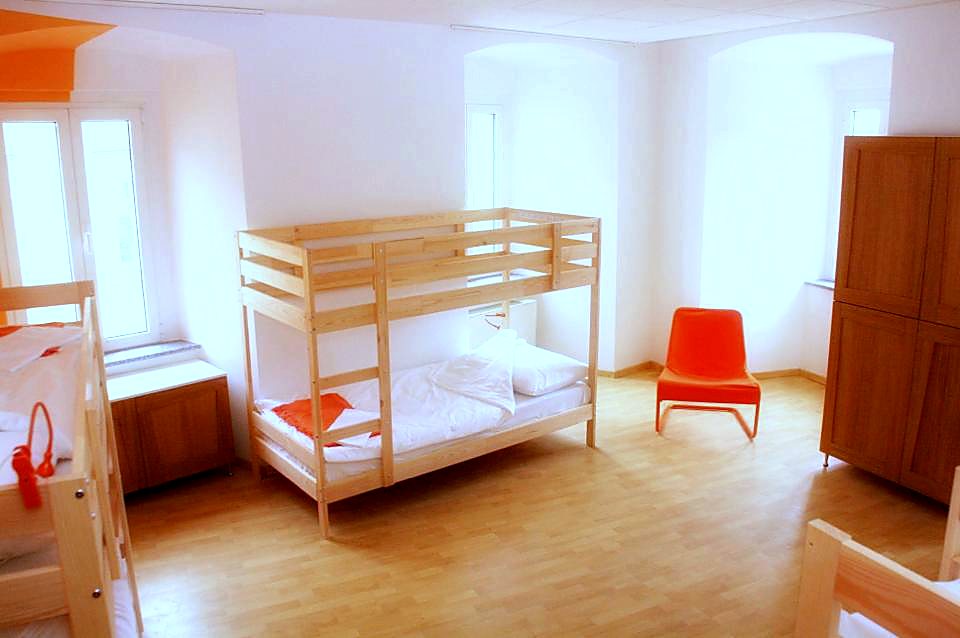 Dorm s drvenim krevetima na kat, ormarom i crvenom stolicom